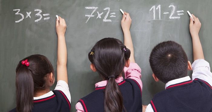 Three school children doing math equations on the blackboard